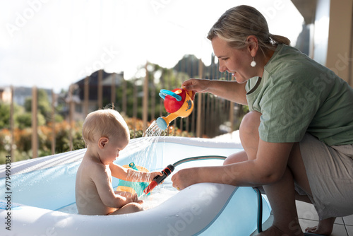 Smiling mother bathing son in inflatable tub at balcony photo