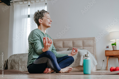 Smiling woman practicing yoga sitting on mat at home