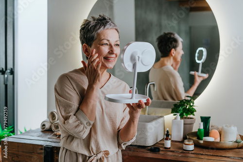 Smiling woman doing skin care looking in mirror at home photo