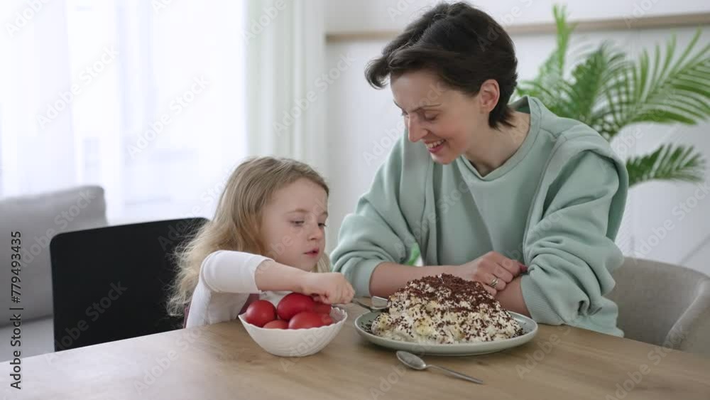 Medium shot with slowmo of beautiful mother and happy little daughter sitting at table and taking dyeing Easter eggs Medium shot with slowmo of beautiful mother and happy little daughter sitting at table and taking dyeing Easter eggs