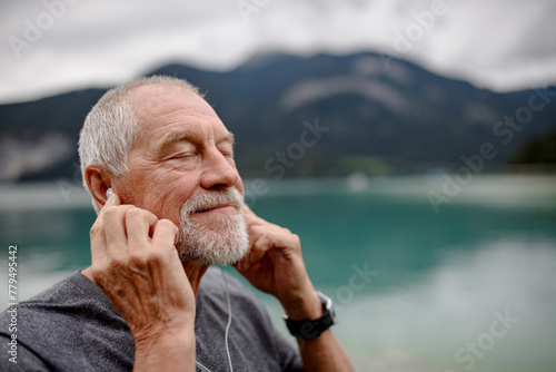 Senior listening music while running by lake in nature. Elderly man exercising to stay healthy, vital, enjoying physical activity and relaxation outdoors. © Halfpoint