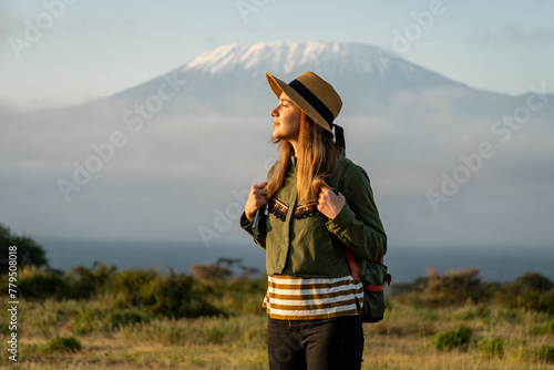 beautiful young girl In a hat stands against the backdrop of the Kilimanjaro volcano and looks away. The concept of tourism and African safari.