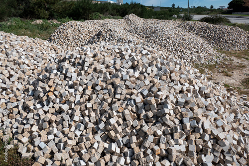 Em meio a um estaleiro na natureza, uma grande pilha de pequenos cubos de granito para o calcetamento de ruas ou passeios photo