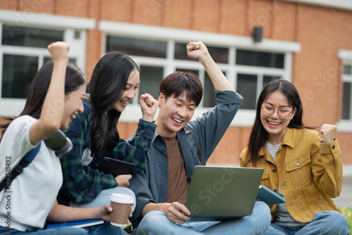 Happy group of college students use laptop feel excited overjoyed triumph with good news over smartphone or Tablet.