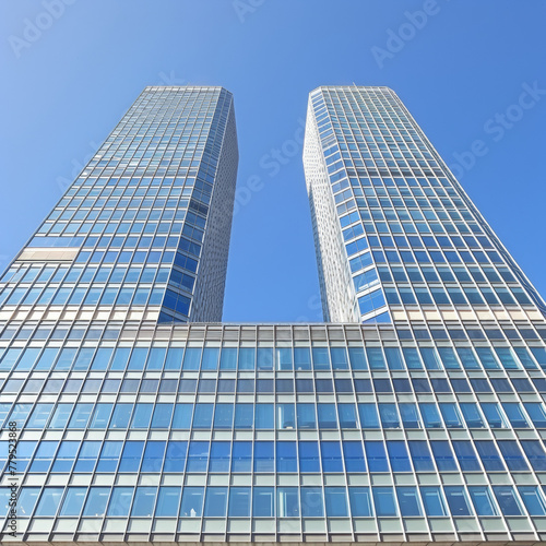 Two tall buildings with many windows and a clear blue sky in the background. The buildings are very tall and have a modern design