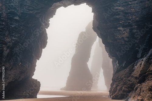 Playa de Las Catedrales in foggy day. Catedrais beach in Ribadeo, Lugo, Galicia, Spain. Natural archs of Cathedrals beach. Moody rock formations on misty day. Travel destination photo