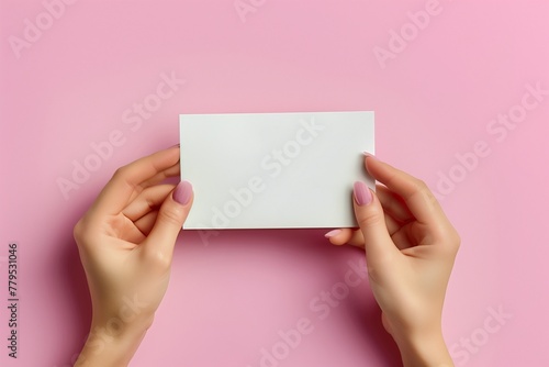 A woman's hands are holding a small empty paper card on a pink background. Postcard mockup template. © Ekaterina Chemakina