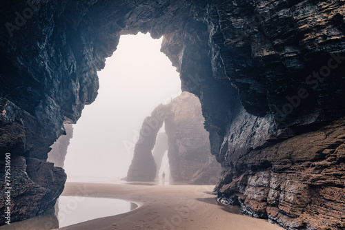 Man standing under natural arch on Cathedrals beach in Galicia, Spainn. Tourist silhouette in foggy landscape with Playa de Las Catedrales Catedrais beach in Ribadeo, Lugo on Cantabrian coast photo