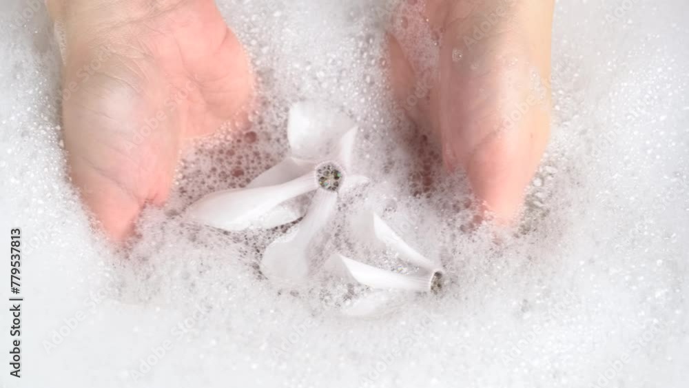 Female hands are washing with soap bubbles and white flowers. SPA concept. Woman plays with fluffy foam in bathtub, macro. Lady holds handful of soap bubbles, close up. Female hands are washing with soap bubbles and white flowers. SPA concept. Woman plays with fluffy foam in bathtub, macro. Lady holds handful of soap bubbles, close up.