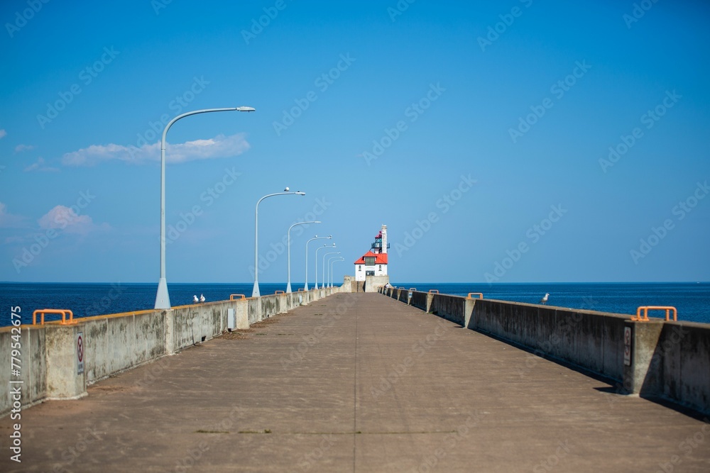 Pavement that leads to a lighthouse captured in coastal North pier on a bright day under a clear sky