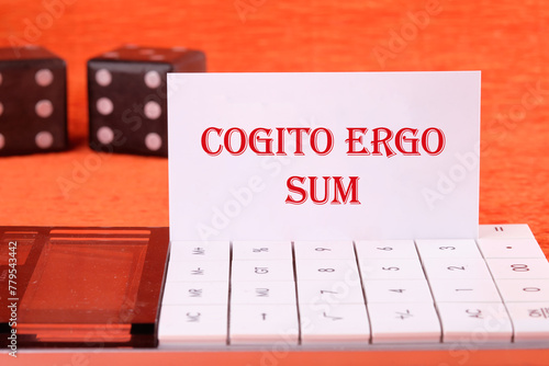 The words Cogito Ergo Sum or I think Therefore I Am on a white business card on a calculator on an orange background