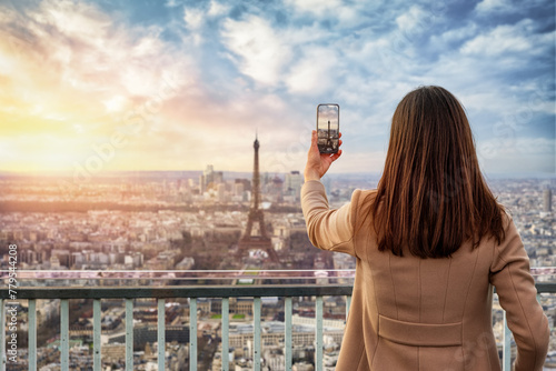 A tourist woman takes pictures with ther phone from the skyline of Paris, France, during sunset time photo