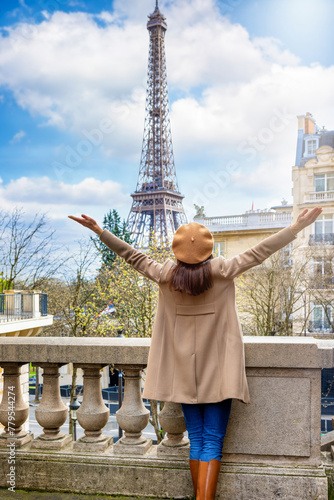 A happy woman with a french beret hat looks at the beautiful cityscape of Paris, France, with Eiffel Tower