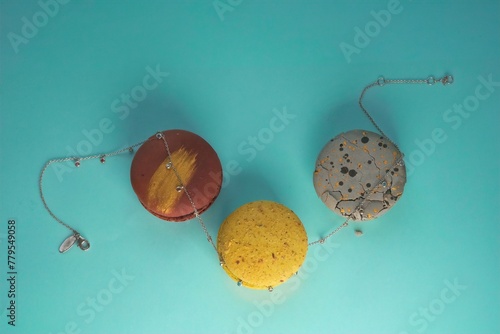 close-up of an elegant silver necklace with a multicolor gemstones between three multicolor macaronies cakes on an azure background