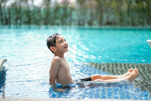 Little Asian kid sitting in pool looking away with smile of happiness.