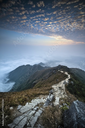Vertical shot of a narrow walkway on top of the big mountains with the clouds in the background