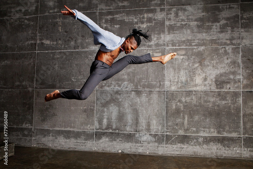 Energetic African American male dancer jumps in splits and stretching, twirls in a studio, executing pirouettes with grace. Black man dancing indoors