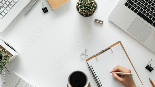 Simple white desktop with one hand writing on a piece of paper with a neutral pen and some note-taking tools on the table