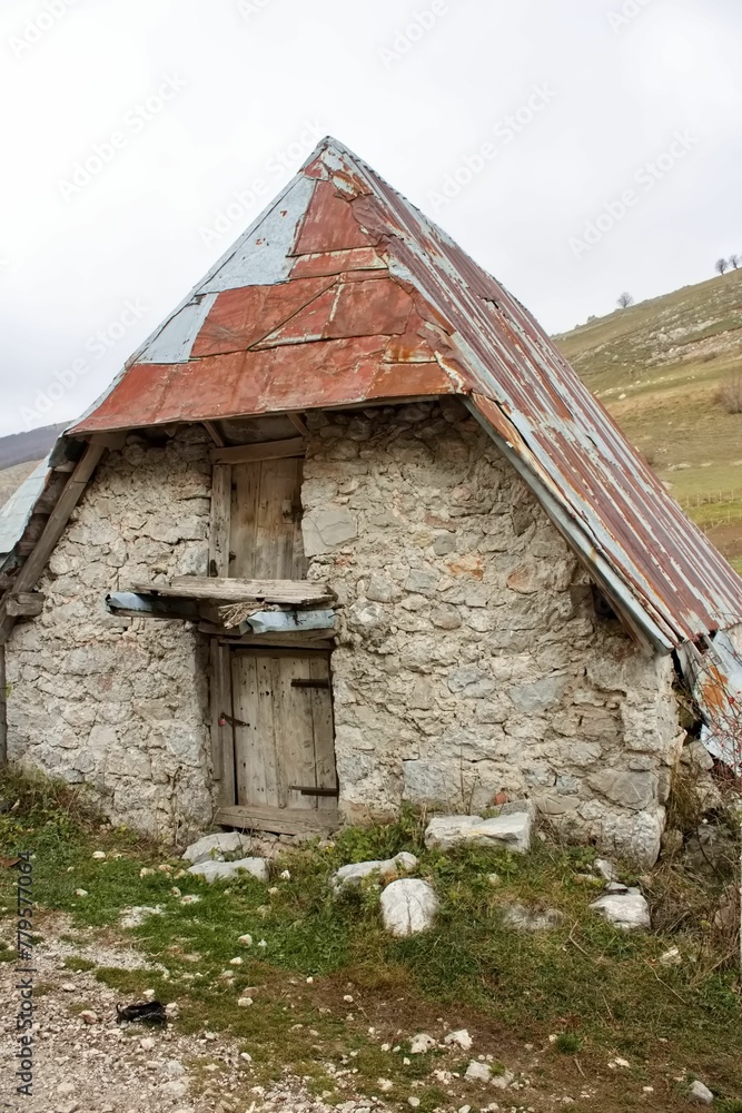 Vertical shot of an old stone building with a rusty metal roof in a rural area Vertical shot of an old stone building with a rusty metal roof in a rural area