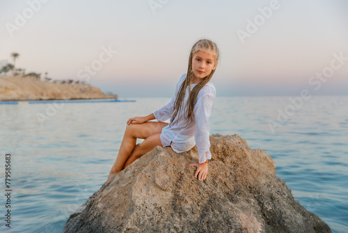 Girl on a stone by the sea at sunset. Calm, peace.