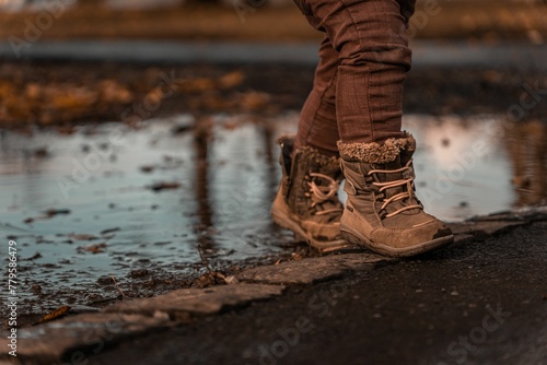 Child standing on the pavement with a puddle in the background on a cold autumn day