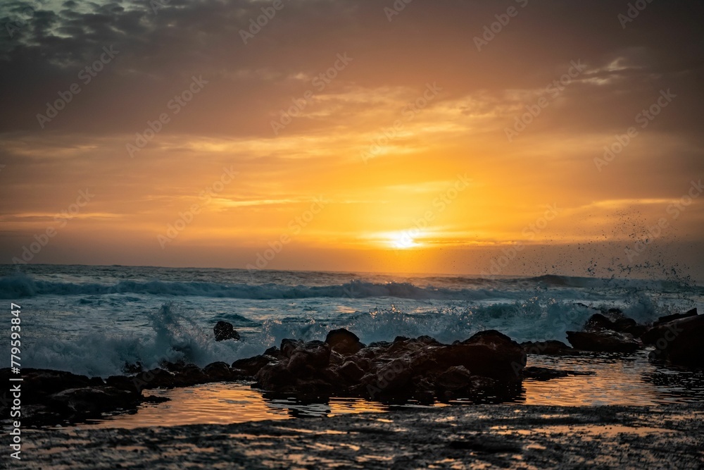 Beautiful golden sunset at a beach with waves hitting the silhouette of rocks on the shore