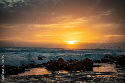 Beautiful golden sunset at a beach with waves hitting the silhouette of rocks on the shore