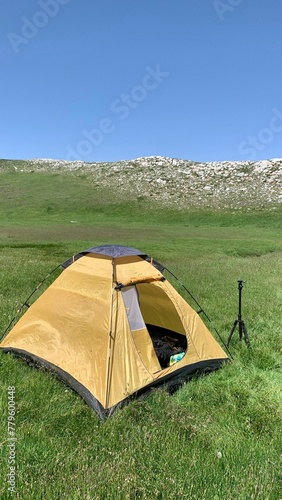 A yellow tent on a green hill, vertical shot
