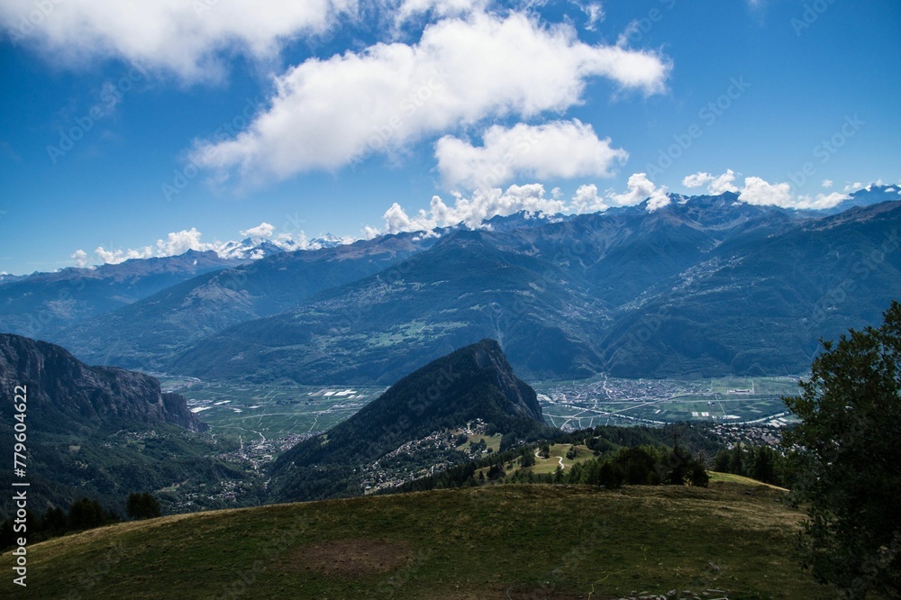 Aerial shot of a rock and a town in the distance in summer in Valais, Switzerland