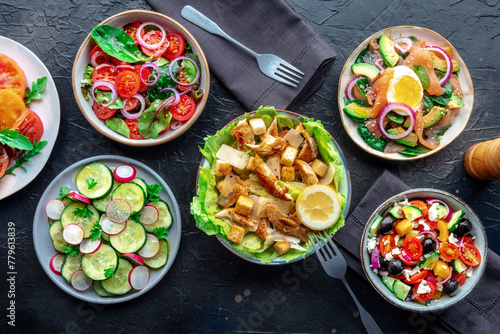 Fresh salads, overhead flat lay shot of an assortment. Variety of plates and bowls with green vegetables. Healthy food, top shot on a black slate background
