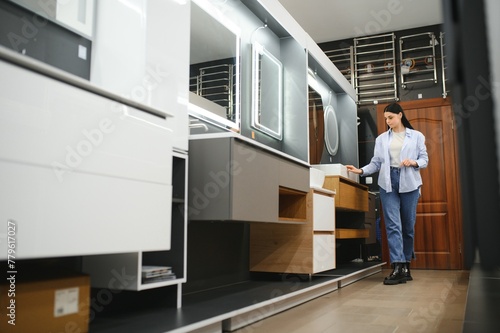 Young woman choosing new bathroom furniture at the plumbing shop with lots of sanitary goods