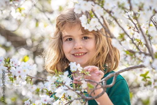 The spring holidays. Happy kid playing under blooming cherry tree with flowers. Kids face near spring blossom nature background. Spring fun. Kid outdoors in a beautiful spring garden.