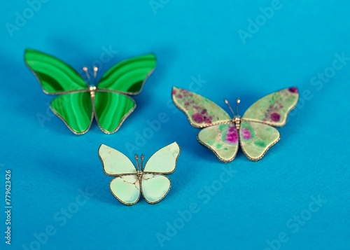close-up of a set of three colorful butterfly-shaped brooches made of semi-precious stones on a bright blue background