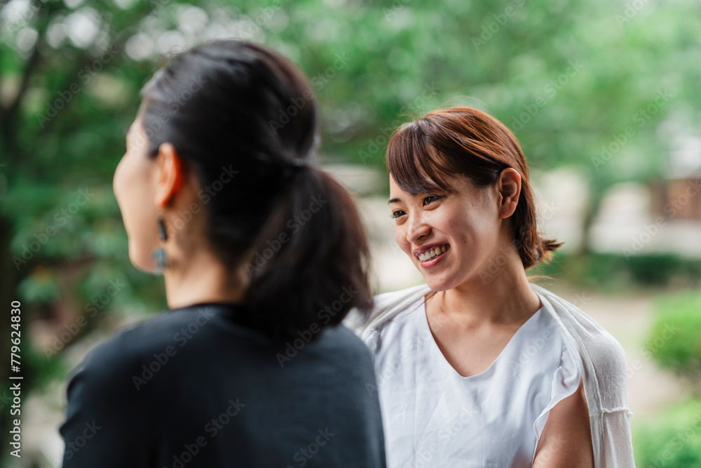 A focused interaction between two Japanese women outdoors, with one in the foreground listening intently to her friend A focused interaction between two Japanese women outdoors, with one in the foreground listening intently to her friend