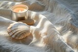 Close-up of a smooth river stone, a seashell, and a lit aromatherapy candle casting soft shadows on a textured linen cloth