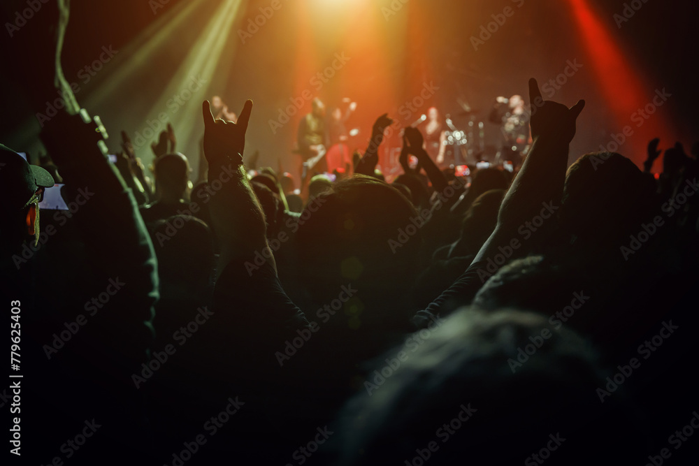 Silhouettes of enthusiastic fans with raised hands are illuminated by the beams of stage lights.