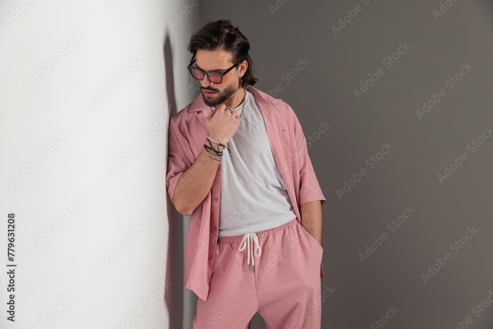 cool casual man with sunglasses holding hand in pocket and looking down