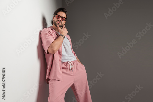 casual fashion man with sunglasses laying on a wall and touching chin