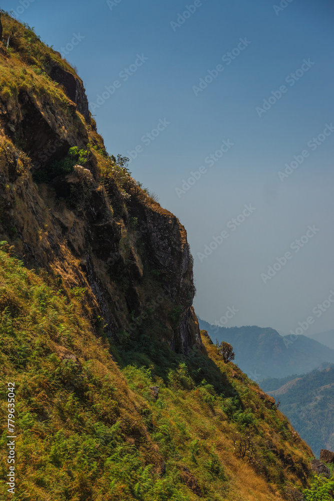 A mountain with a rocky cliff and a lush green hillside