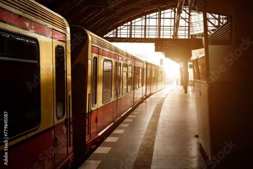 The red and yellow train stands on the empty platform of the train station during golden sunset hour