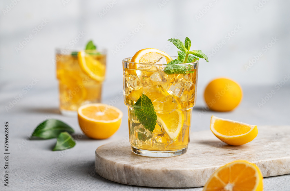 Two glasses with iced drink with lemon and mint on a marble board on a light background with shadow and citrus fruits. Two glasses with iced drink with lemon and mint on a marble board on a light background with shadow and citrus fruits.