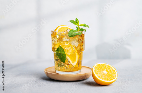 Iced tea with lemon, mint in a glass on light background with shadow and citrus fruits.