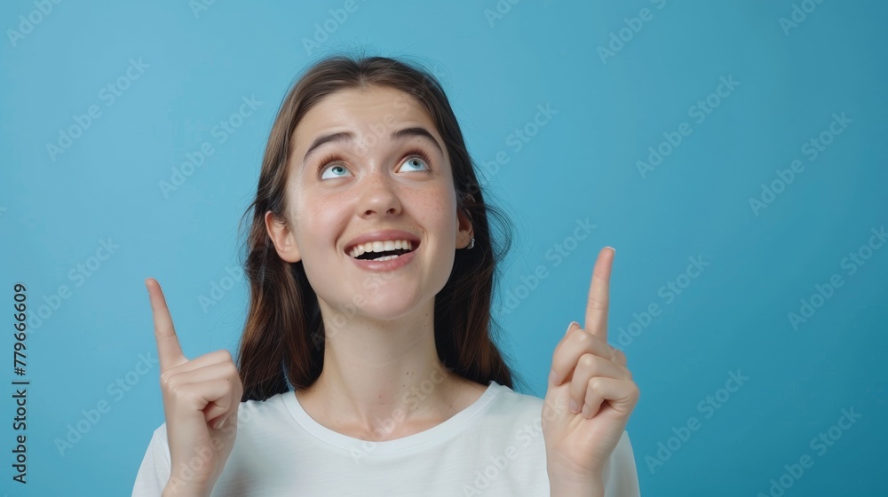 Portrait of a beautiful and cheerful young American woman smiling and pointing up isolated on blue background, template for advertising or promotion, with copy space for text Portrait of a beautiful and cheerful young American woman smiling and pointing up isolated on blue background, template for advertising or promotion, with copy space for text