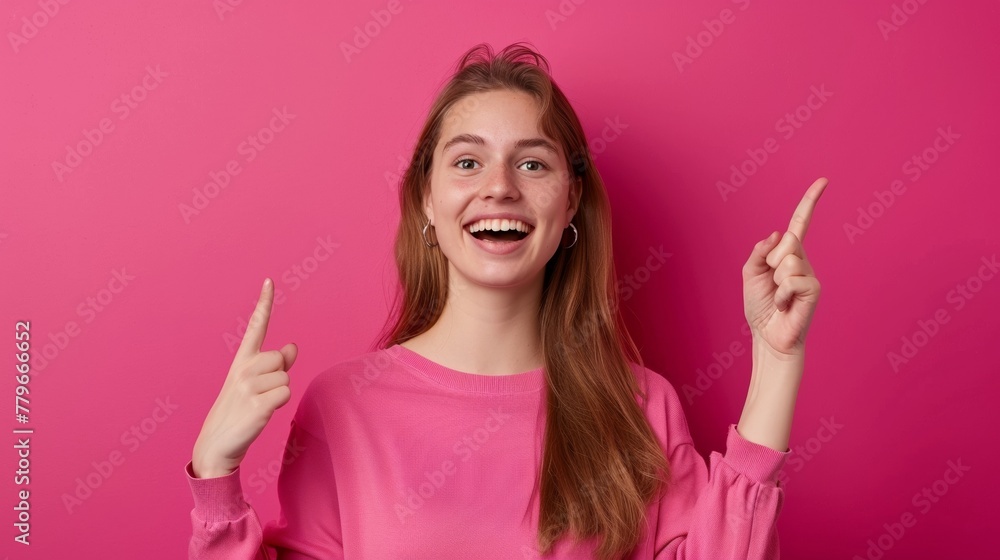 Portrait of a happy beautiful young American woman wearing a casual outfit pointing up isolated over a magenta background, template for advertising or promotion, with copy space for text Portrait of a happy beautiful young American woman wearing a casual outfit pointing up isolated over a magenta background, template for advertising or promotion, with copy space for text