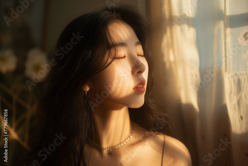 A serene young asian woman enjoys a moment of tranquility as the morning sun caresses her face through sheer curtains.