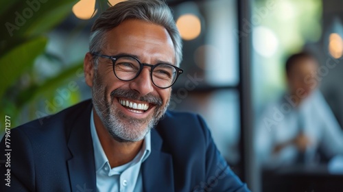 Happy bearded man smiling while sitting at a table in an office wearing glasses