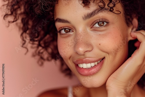 Skin care. Woman with beauty face touching healthy facial skin portrait. Beautiful smiling girl model with curly hair and natural makeup touching glowing hydrated skin on pink background closeup