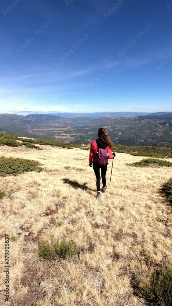 Woman walking on top of the Peñalara mountain, next to the Laguna de los Pajaros, in the Sierra de Guadarrama, with a large valley in front, in Madrid, Spain. Vertical video