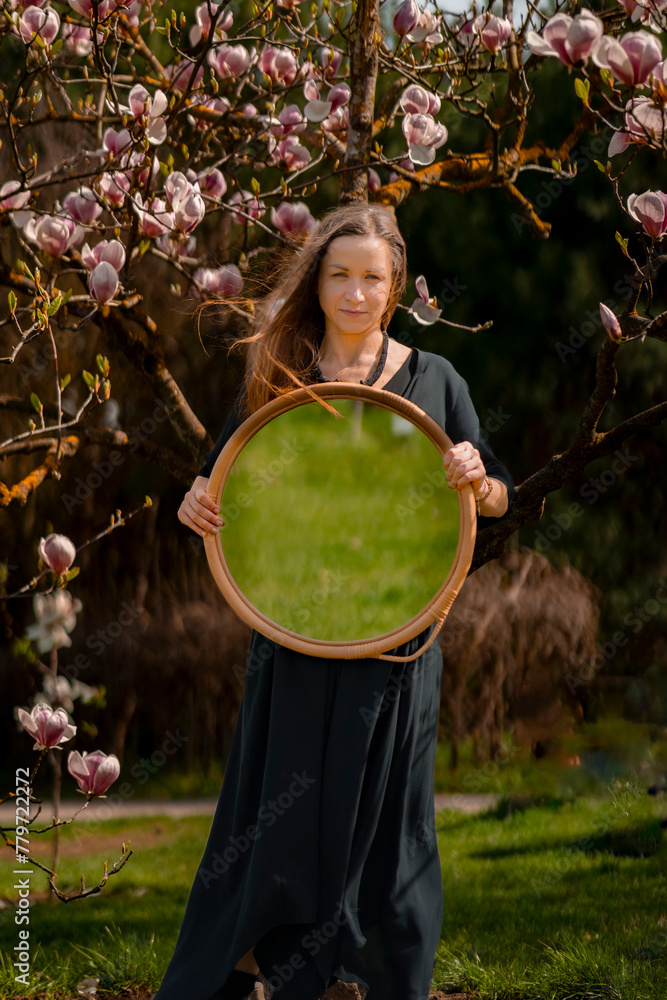 Girl Standing by Magnolia Tree with Round Mirror Reflecting Green Grass