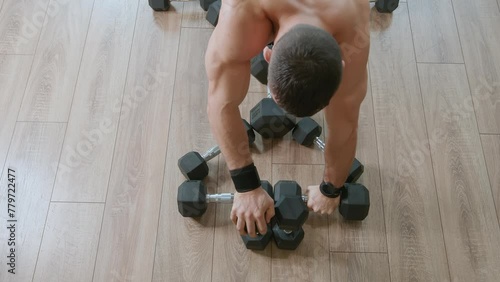 Young man with a naked torso does push-ups from dumbbells lying on floor and pumps muscles of chest, back and triceps. Load on core muscles and anterior deltoid muscles photo